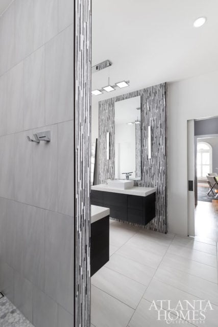 Modern bathroom with a dark wood vanity, white countertop, vessel sink, and a vertical striped mosaic tile accent wall. Light gray tiled floors and walls.