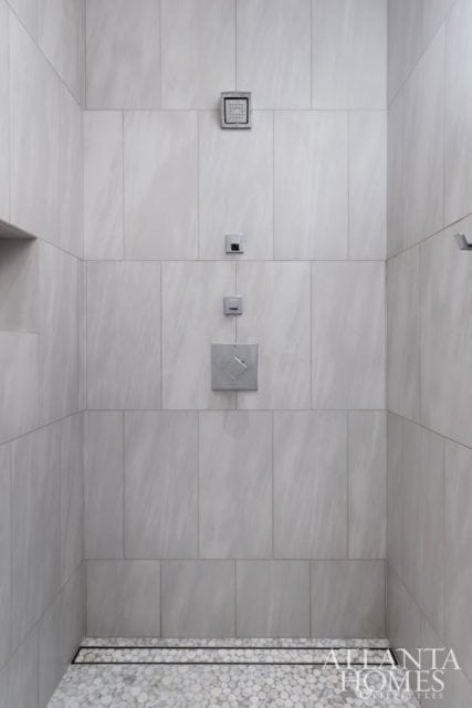 Modern shower with light gray tiled walls, multiple shower heads, and a pebble tile floor with a linear drain.