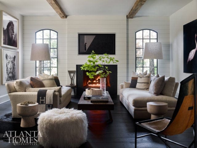 Living room with shiplap walls, exposed beams, fireplace, two sofas, and artwork of animals.