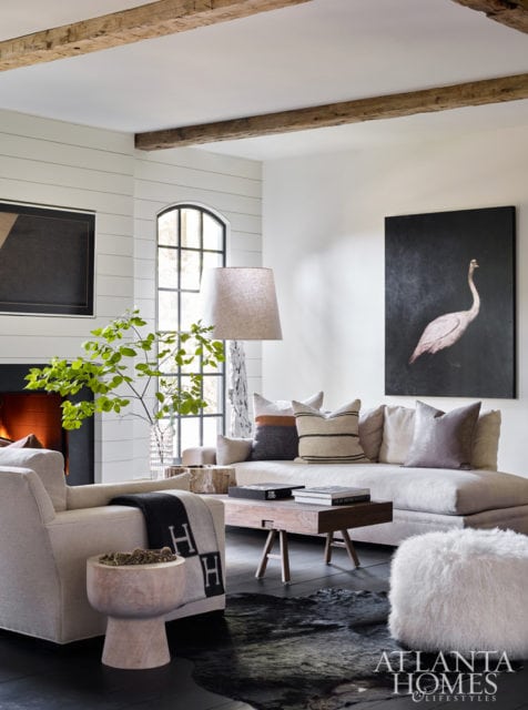 Living room with shiplap walls, exposed wooden beams, sectional sofa with patterned pillows, artwork of a crane, and a fireplace.