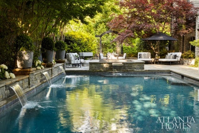 Swimming pool with cascading waterfalls, surrounded by lush greenery, stone patio, and outdoor seating.