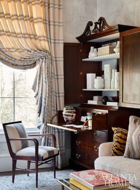 Desk area with a dark wood secretary desk, striped curtains, a patterned armchair, and a sofa with a tiger print pillow.