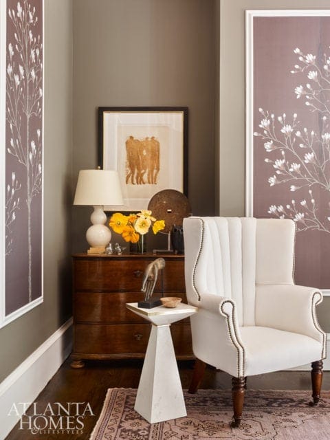 Living room corner with a white upholstered wingback chair, a wooden dresser, and decorative artwork on the walls.