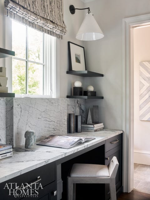 Desk area with a marble countertop, dark wood cabinetry, and a stool with a patterned seat. A window with a patterned roman shade is to the left.