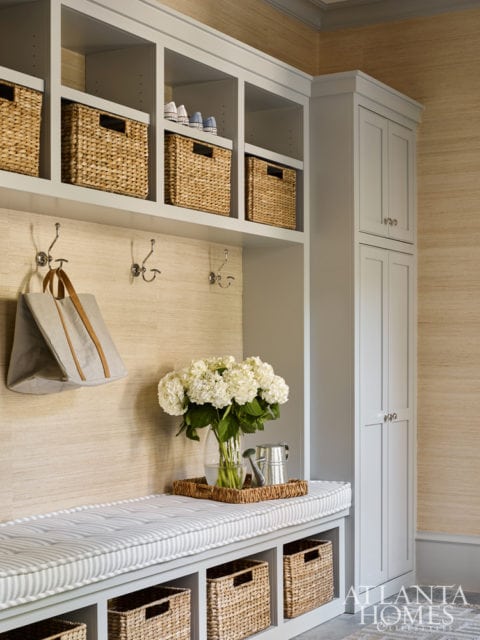 Mudroom with built-in gray cabinetry, woven storage baskets, a striped bench cushion, and a vase of white hydrangeas on a woven tray.