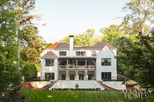 White brick house with multiple levels of balconies, dark-framed windows, and a copper roof, surrounded by lush green trees and manicured lawn.