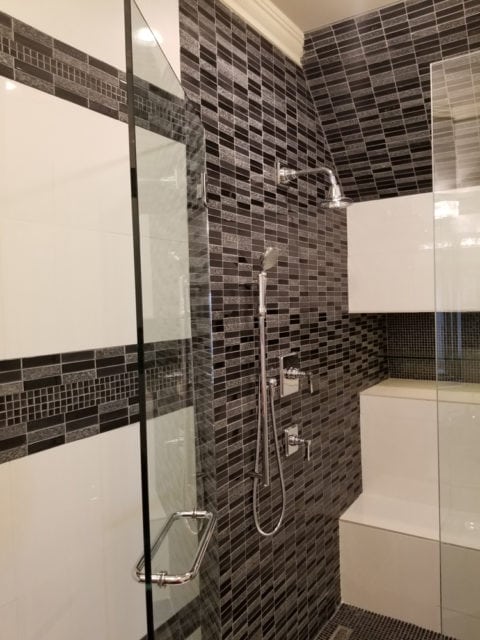 Modern bathroom with a glass-enclosed shower featuring black and white mosaic tile walls, chrome fixtures, and a built-in white bench.