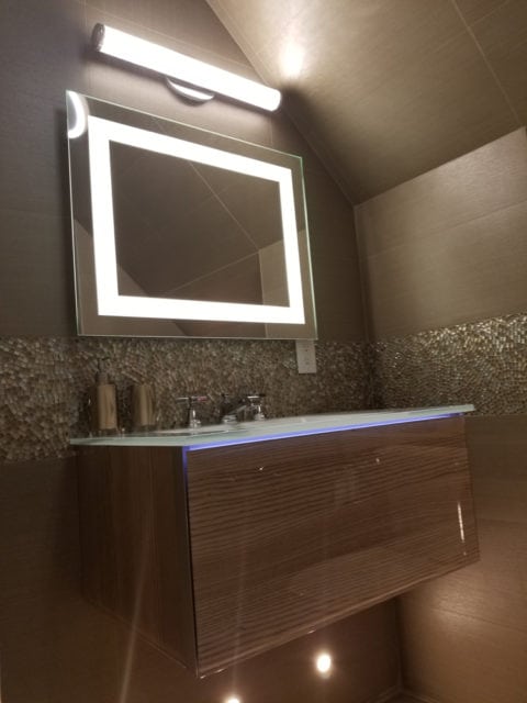 Modern bathroom with a floating wood vanity, illuminated mirror, and mosaic tile backsplash.