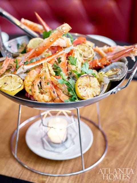 Seafood platter with king crab legs, shrimp, oysters, and grilled lemon slices, garnished with parsley, served in a metal chafing dish over a lit candle.