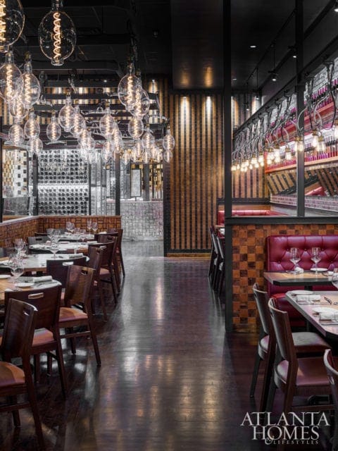 Restaurant dining room with dark wood floors, red leather booths, and numerous Edison bulb pendant lights hanging from the ceiling.