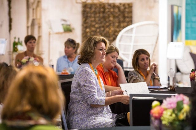 Women sitting at tables, listening and taking notes during a presentation or conference.