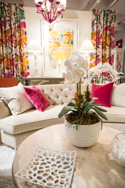 Living room with a tufted sofa, patterned curtains, abstract art, and a marble coffee table with a white orchid centerpiece.