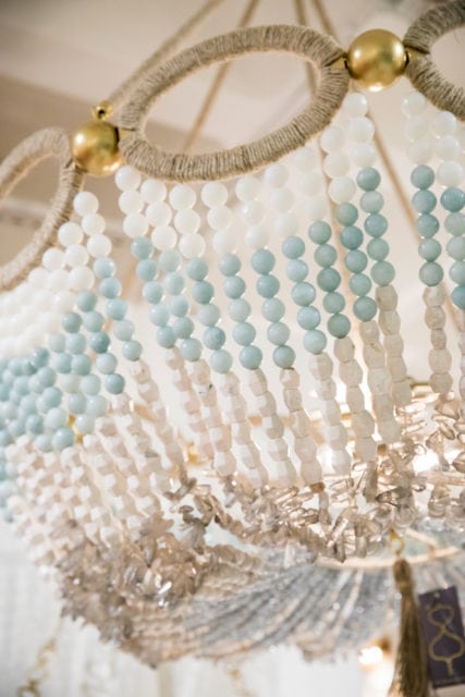 Close-up of a chandelier with strands of white, light blue, and clear beads, accented with gold hardware and rope detail.