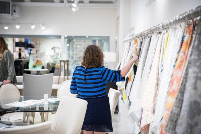 Woman in blue and black striped shirt browsing fabric swatches hanging on a rack in a showroom.