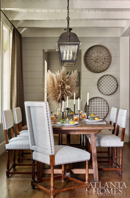 Open to the kitchen, the dining area features a double lantern light fixture by Paul Ferrante through Ainsworth-Noah. Grain sifters from Nicholson Gallery have been repurposed as artful accents. The chairs are from Jerry Pair and the table is custom.