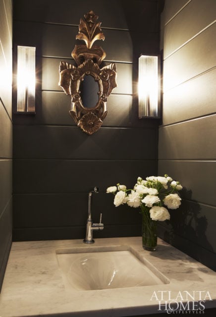 The powder bathroom is moody thanks to a dark, handsome hue and a French mirror.