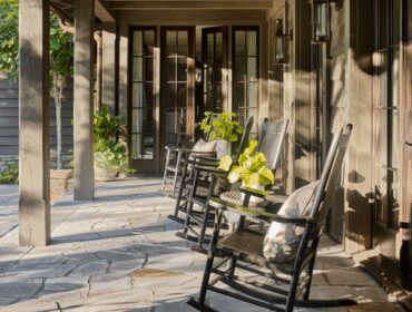 Porch with rocking chairs and stone patio, featuring dark wood siding and French doors.