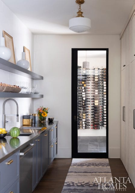 The butler’s pantry corridor reveals both builder Siegel Construction & Design’s astute finish selections—like steel-blue cabinets and antiqued brass—and its knack for lighting, like this vintage-inspired pendant in white glass. The climate-controlled wine cellar comes in handy for the homeowners, who enjoy collecting.