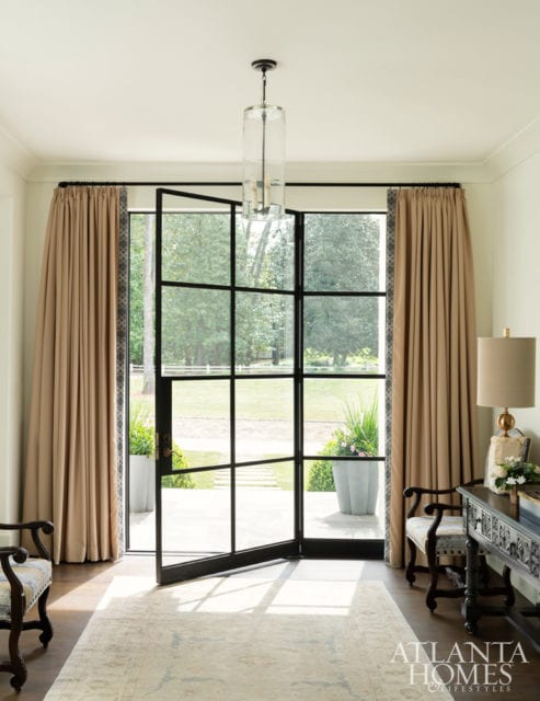 Bradley softened the steel-and-glass front entry with latte-toned drapery panels. The drapery fabric is by Mokum, through Paul+, and the trim is Samuel & Sons trim. The Pendant is from South of Market, the table lamp is Noir, and the Oushak rug is Designer Carpets.