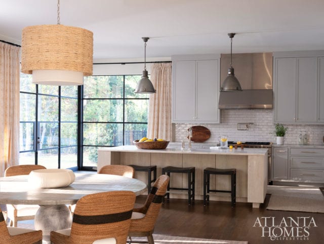 In the farmhouse-inspired kitchen, a trio of Palecek counter stools sidles up to an island anchored by bleached white oak, while stainless steel accents—a simple hood and a pair of coordinating pendants (Circa Lighting’s Fulton style in Industrial Steel)—offer a utilitarian feel. The floral fabric used for the drapery panels is a Kerry Joyce design, and the natural-fiber pendant over the breakfast table is the Amani Drum from Made Goods.
