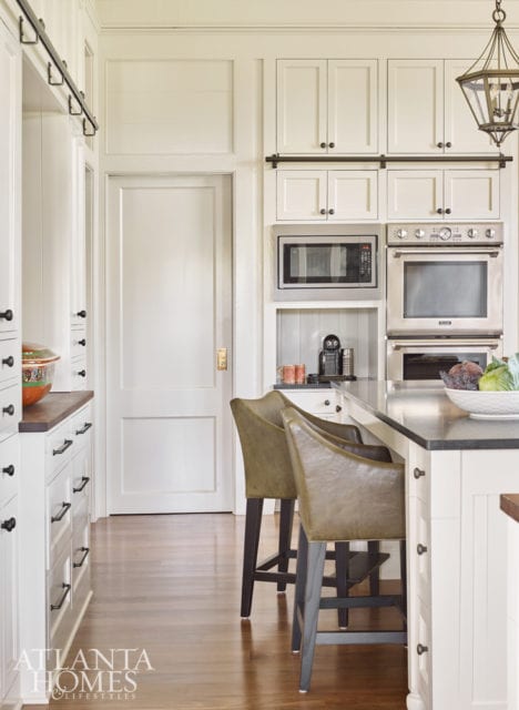 Storage was a priority for the client, who has both inherited and collected many dish and serveware pieces over the years. The solution came in the form of top-to-bottom cabinetry in the kitchen that can be accessed via a ladder. Barstools in a green leather by Lee Industries add a subtle hint of color. The lantern is from Urban Electric Co.