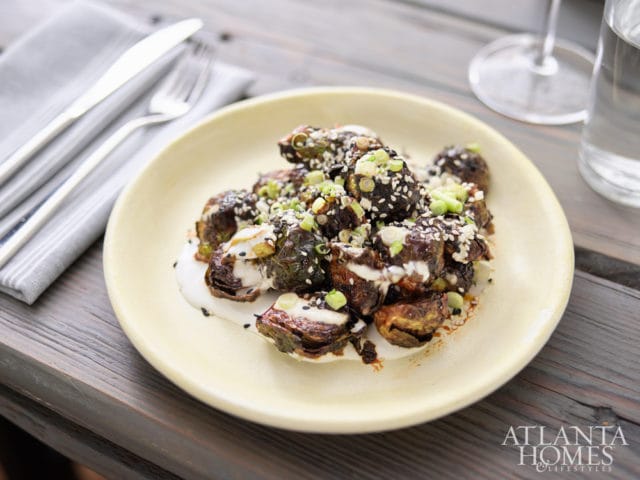 Roasted Brussels sprouts with white sauce, sesame seeds, and chopped green onions on a pale yellow plate.