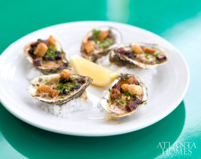 Oysters Rockefeller topped with croutons and herbs, served on a white plate with a lemon wedge and coarse salt.