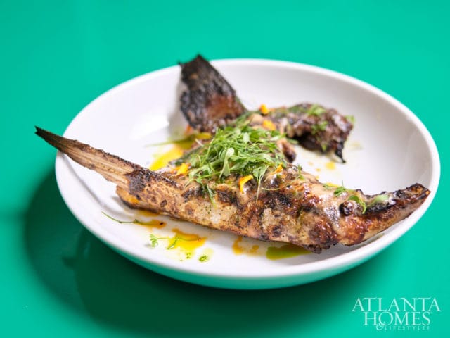Grilled fish with herbs and sauce on a white plate, with the Atlanta Homes & Lifestyles logo in the bottom right corner.
