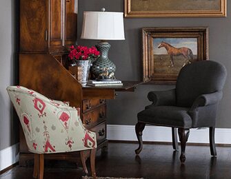 Two armchairs in a room with a wooden desk, lamp, and horse painting.