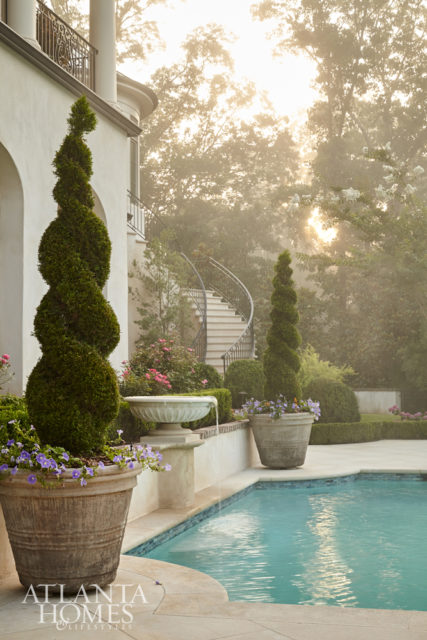 Early morning mist envelopes the outdoor living area, which includes a quatrefoil-shaped pool and boxwood hedges separating the pool from the surrounding gardens.