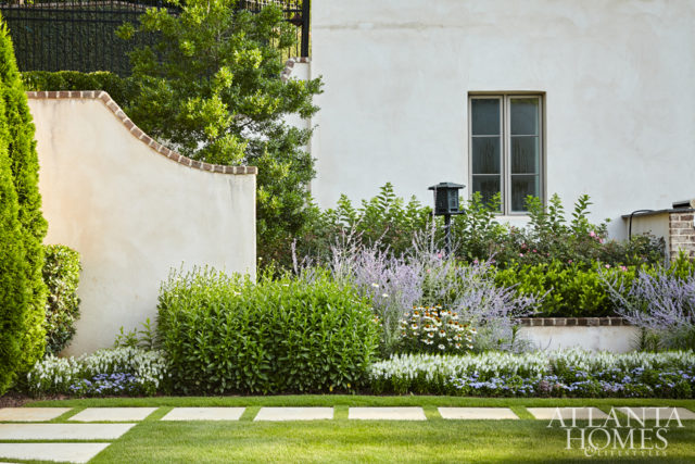The outdoor area is framed by plantings, including English-style perennial borders set against the stucco and brick exterior.