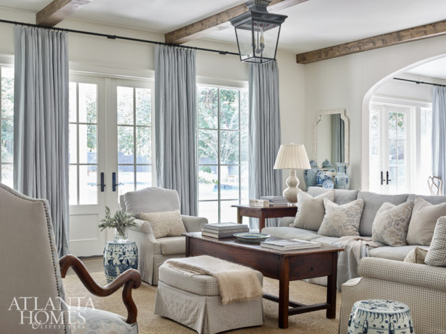 Built-in bookcases with lattice detailing flank the limestone fireplace by Francois & Co., which is topped by a lively abstract painting. “We wanted the family den to blend seamlessly with the look of the kitchen and breakfast room, so we used the same fabrics in soft neutral shades of blue and taupe,” says DeLoach.