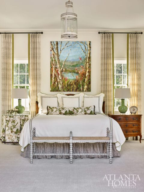 Bedroom with a king-size bed, white bedding, botanical print pillows, a landscape painting, green lamps, and floral patterned nightstands.