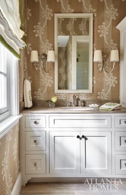 Powder room with brown and cream damask wallpaper, white vanity with marble countertop, silver faucet, and double sconce lighting.