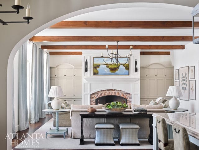 Living room with a white fireplace, exposed wooden beams, built-in cabinetry, and light blue striped curtains.