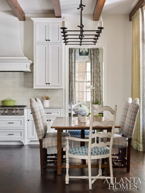 Dining area with white cabinetry, a wooden table, and chairs upholstered in plaid and blue patterned fabric. Exposed wooden beams are visible on the ceiling.
