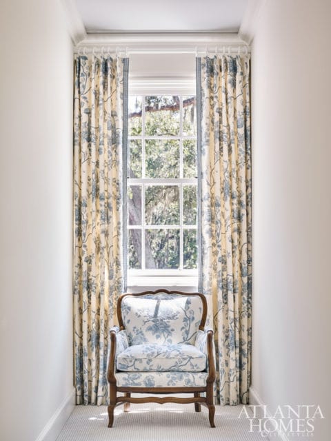 Armchair upholstered in blue and white floral fabric in front of a window with matching floral curtains.