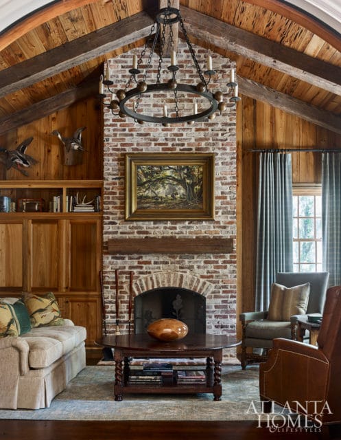 Living room with vaulted wood-paneled ceiling, brick fireplace, tufted sofa, leather armchairs, and a dark wood coffee table.