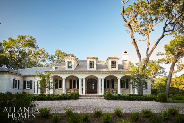 Southern-style home with white siding, brick accents, and a covered porch with columns. Surrounded by mature trees and a brick driveway.