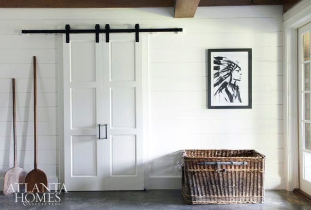 White paneled double doors with black barn door hardware, framed black and white artwork of a Native American profile, and a large wicker basket