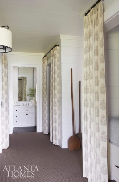 Hallway with shiplap walls, patterned curtains, and a glimpse of a white vanity in a bathroom.