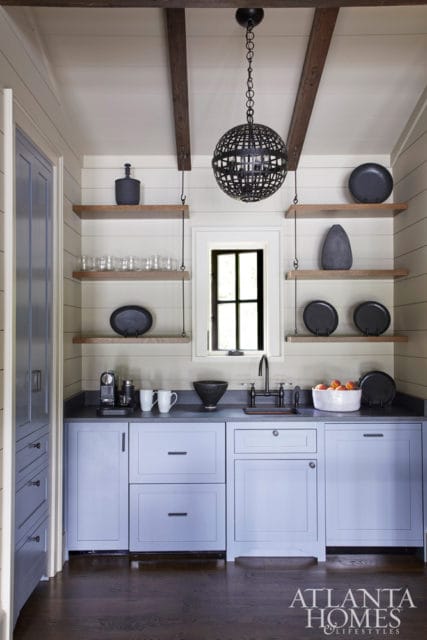 Pale blue kitchen cabinets with dark gray countertops, open wooden shelves, and a black orb chandelier.