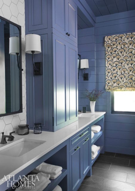 Blue bathroom with white quartz vanity, hexagonal tile backsplash, and shiplap walls. Features a tall cabinet, wall sconces, and a patterned roman shade.