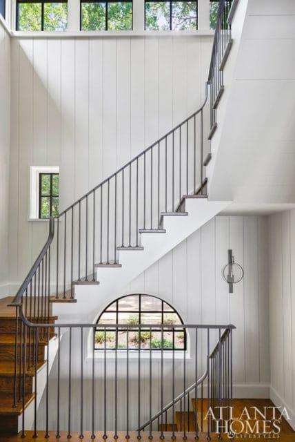 White paneled staircase with dark metal railings, wood treads, and a large arched window overlooking greenery.