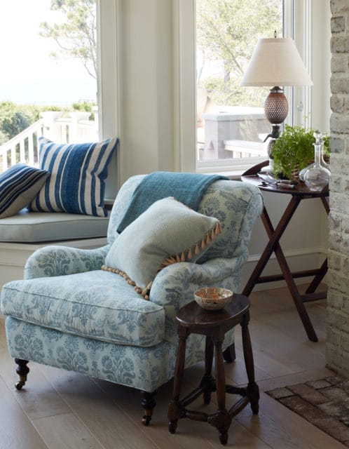Armchair upholstered in light blue damask fabric with blue and white striped pillows on a window seat. A teal throw blanket is draped over the armchair.