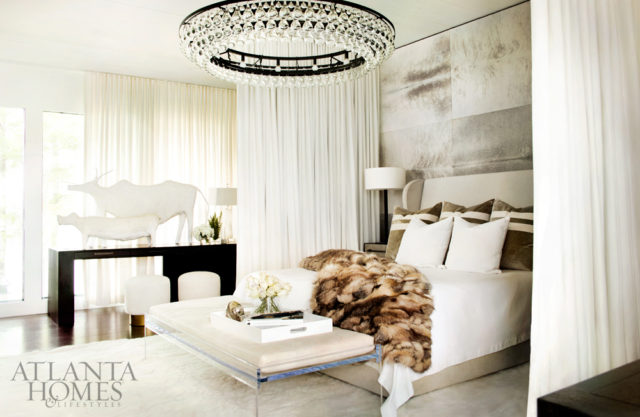 In the master bedroom, with its billowing curtains, walls swathed in hide and a floating mirror, an Ochre chandelier from R Hughes adds another note of glamour. The custom ottoman is by Pfeifer Studio. French animal sculptures, South of Market.