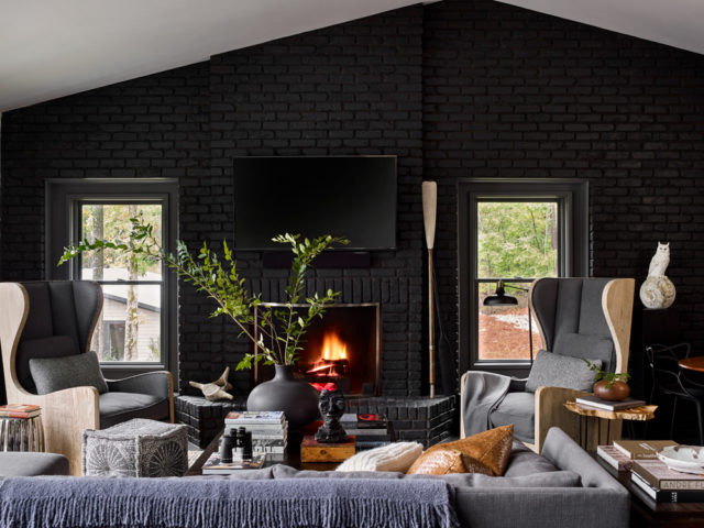 A black stain was applied to the hunt cabin’s original brick walls to lend contemporary verve. The wingback chairs from Swoox were a jumping point for the interiors. The gray vessel is from B.D. Jeffries; the woven pillows are from Townhouse; and the throws and white knit pillow are Holland & Sherry.