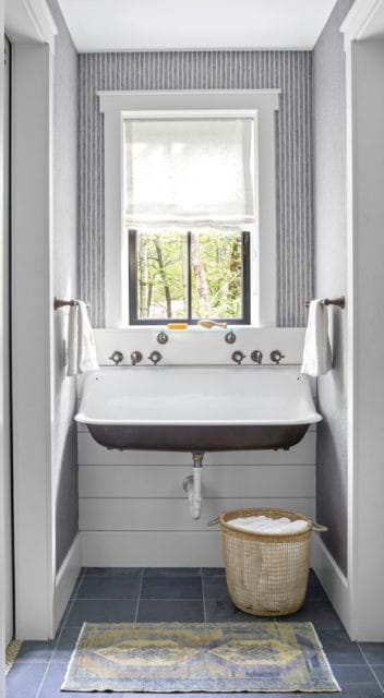 Bathroom with a large white sink, striped grey wallpaper, shiplap wainscoting, and a window overlooking trees.