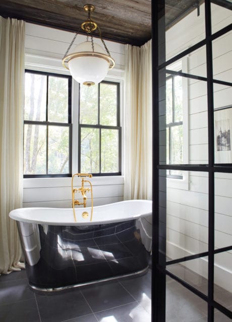 Bathroom with a freestanding black clawfoot tub, gold faucet, and large windows with sheer curtains. A modern globe pendant light hangs from a wood-paneled ceiling.