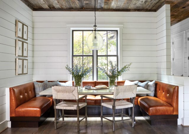 Dining nook with brown leather tufted banquette seating, light wood plank ceiling, shiplap walls, and two woven-seat chairs at a table.